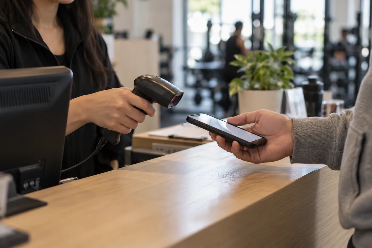 A member holds up the QR pass on their phone to a handheld scanner at the counter